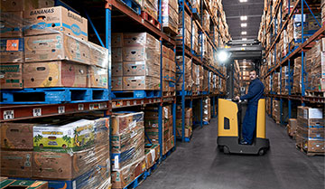 Operator in Cat pantograph reach truck in narrow aisle of boxes